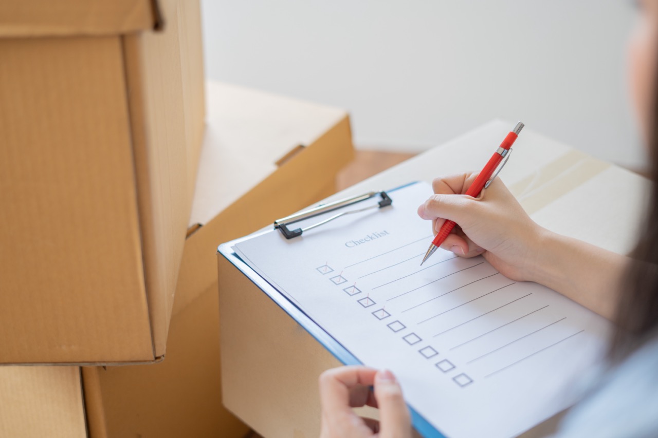 Mover checking a relocation checklist among packed moving boxes